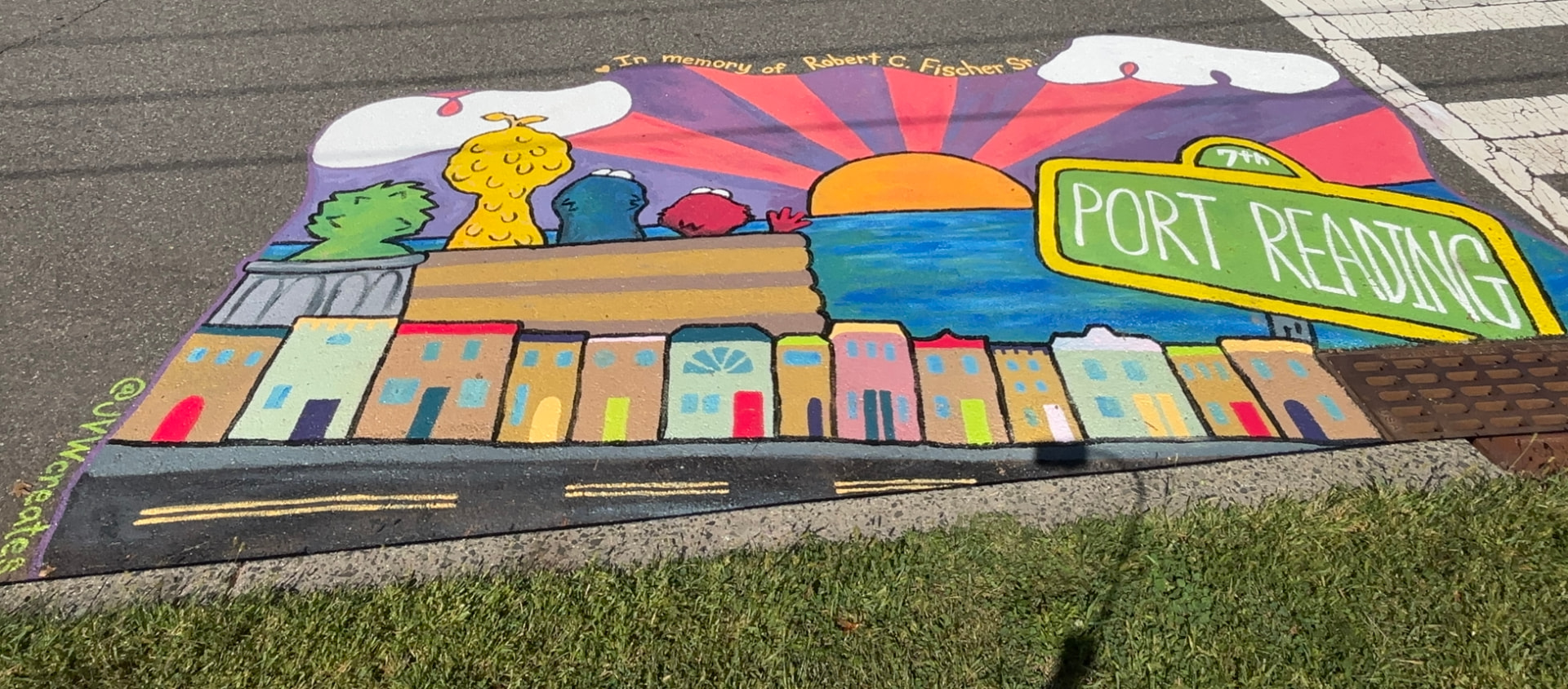 Street mural of the Port Reading waterfront with colorful rowhouses, a sunset over the water and a green Port Reading street sign