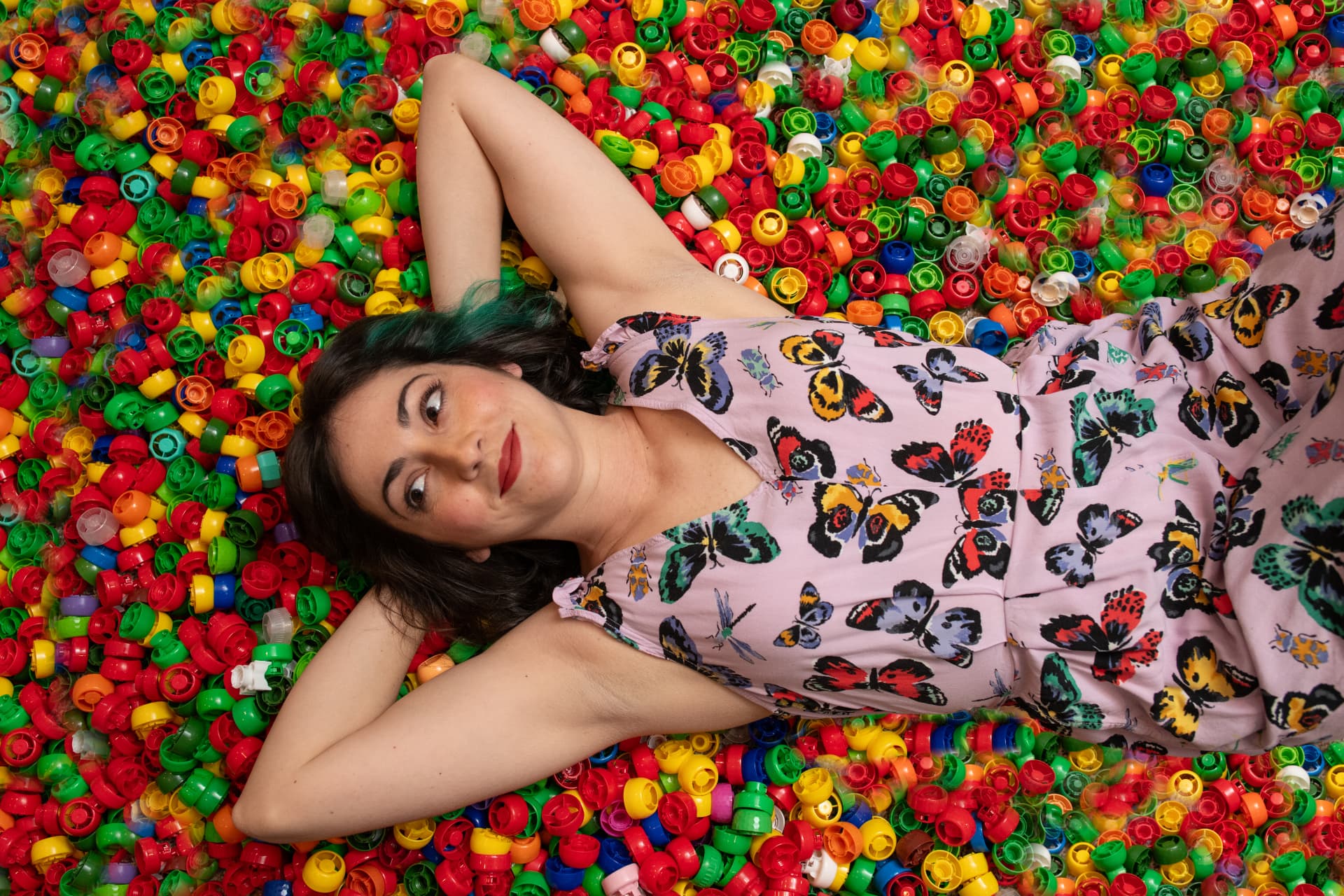 Julia lying back in a colorful pit of rescued bottle caps