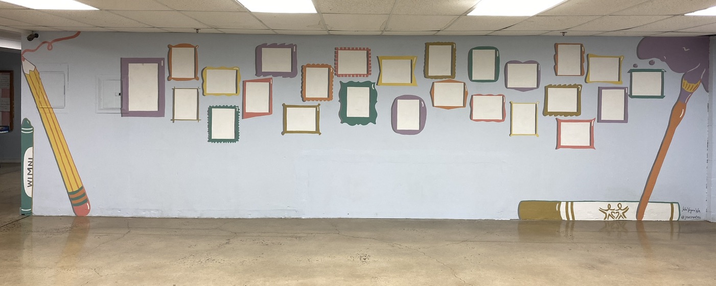 Indoor mural of empty painted picture frames flanked by a giant pencil, crayon and paintbrush, made as a display wall for student art