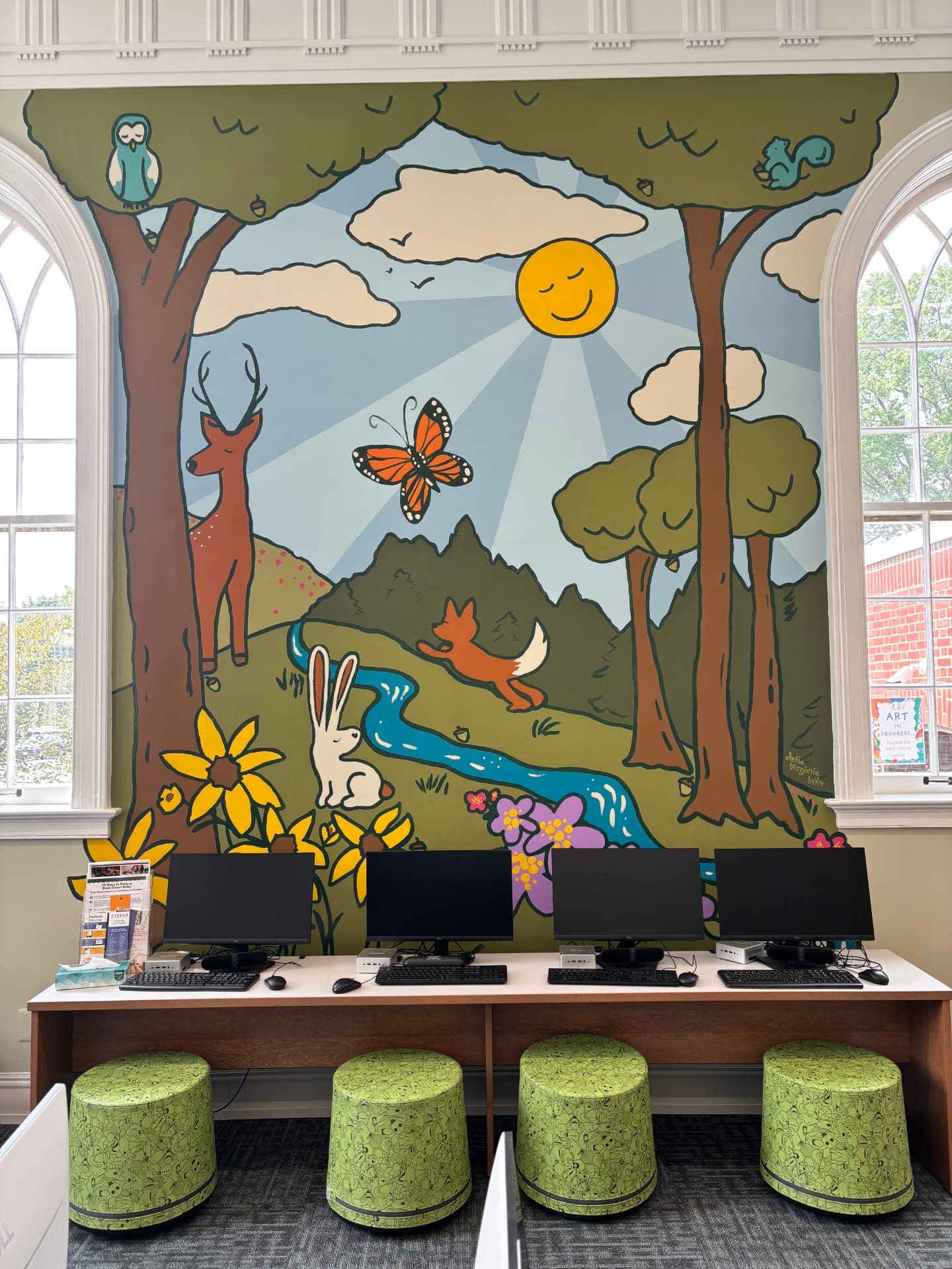Cheerful woodland library mural with a deer, fox, rabbit, monarch butterfly, owl, squirrel, smiling sun and winding blue river