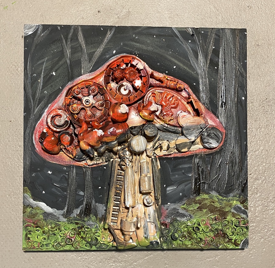 Red-capped mushroom sculpted from recycled plastic and metal parts in a dark painted forest with moss made from can tabs