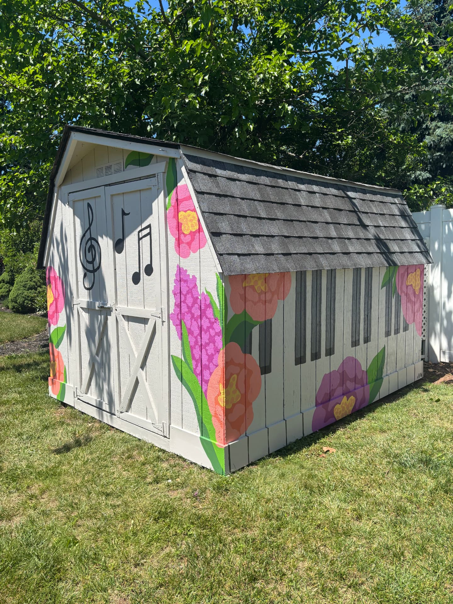 Backyard shed painted with oversized pink and coral flowers, green leaves, music notes and piano keys on its walls