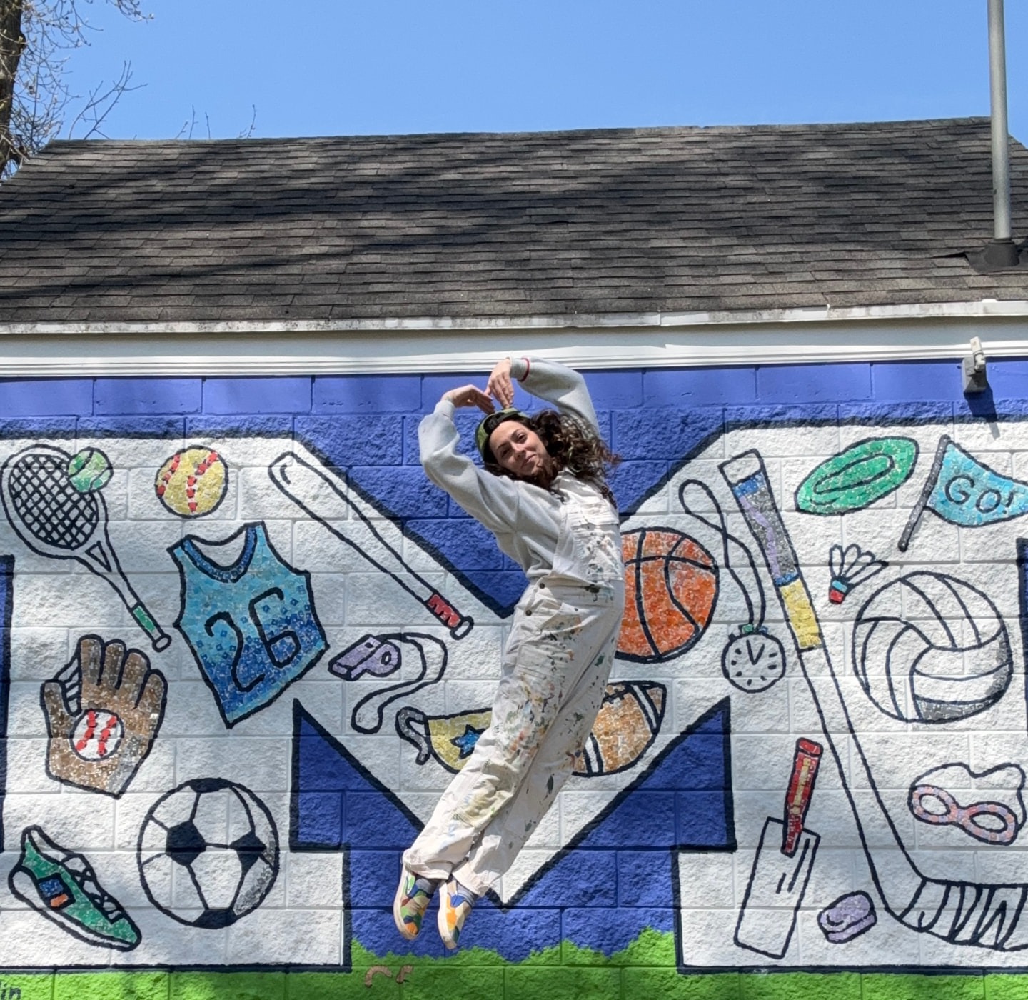 Julia leaping in front of a sports-themed mural painted with tennis, baseball, basketball, soccer and hockey icons