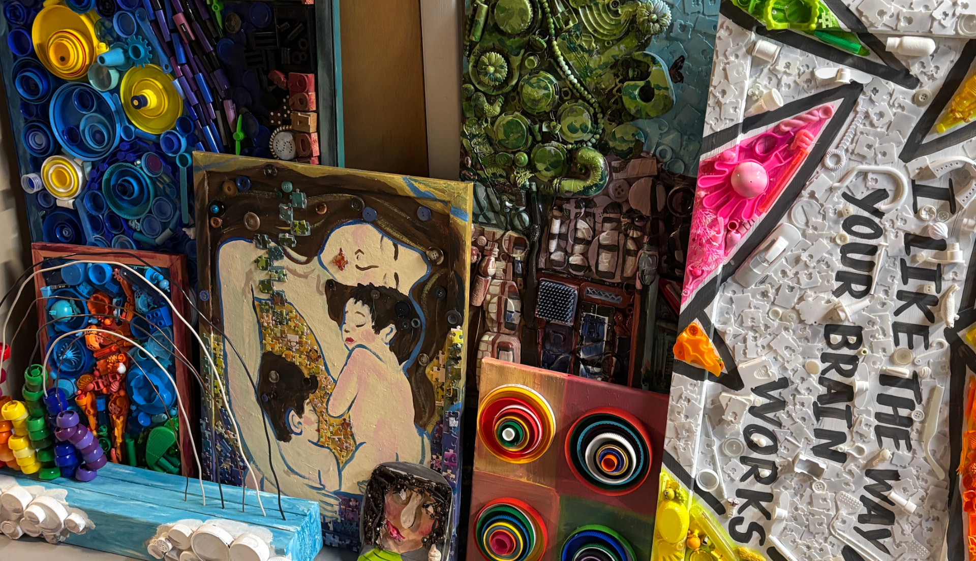 A studio wall of colorful reuse artworks made from bottle caps, marker caps and found materials