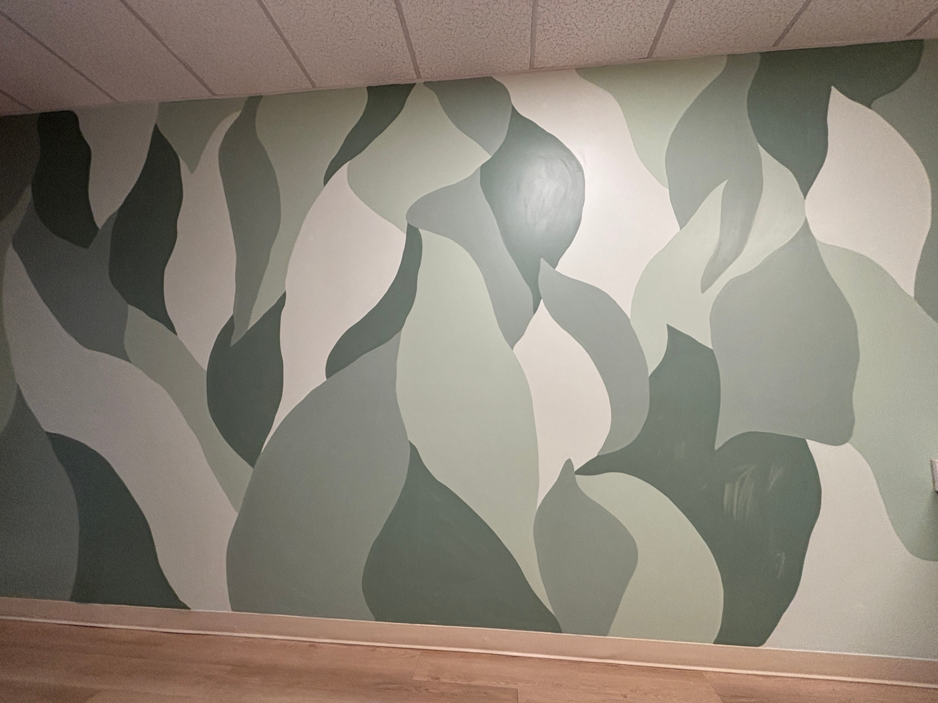 Interior wall mural of flowing abstract leaf shapes in layered sage and forest green tones
