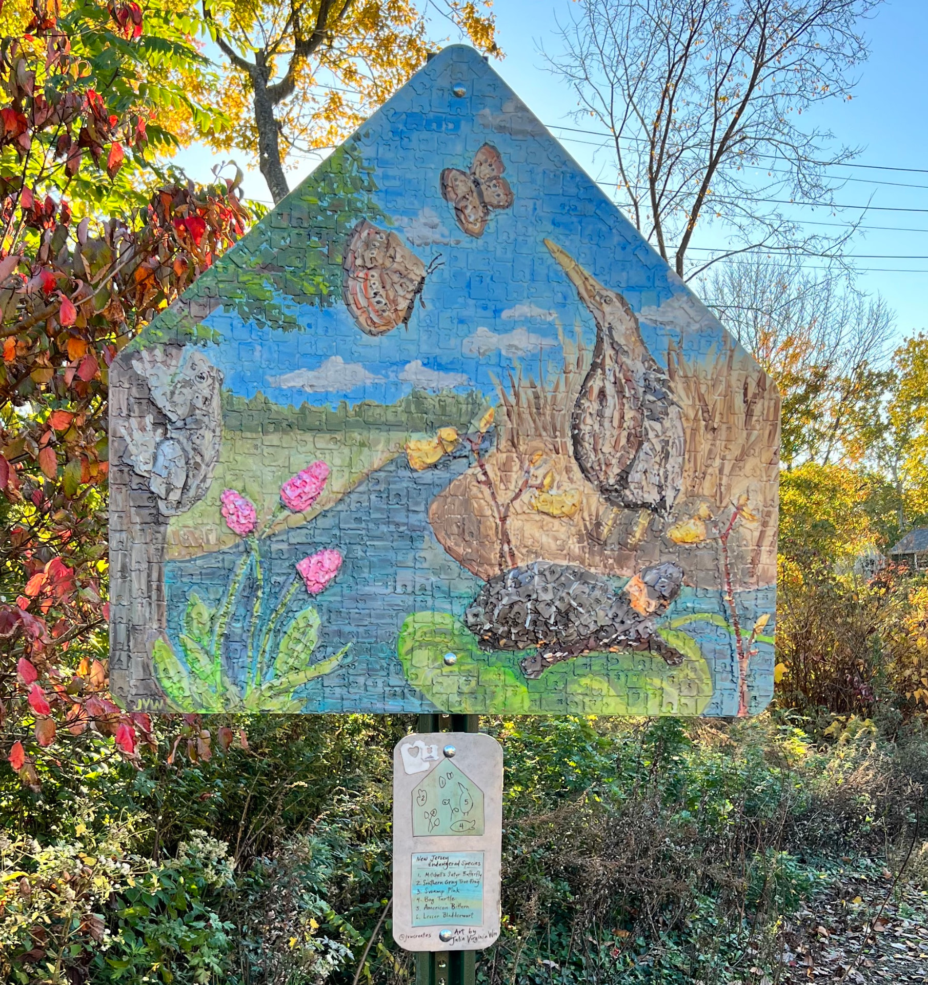 Triangular recycled street sign mural depicting endangered New Jersey species — butterfly, tree frog, bog turtle and bittern — made from reused bread tags and found materials