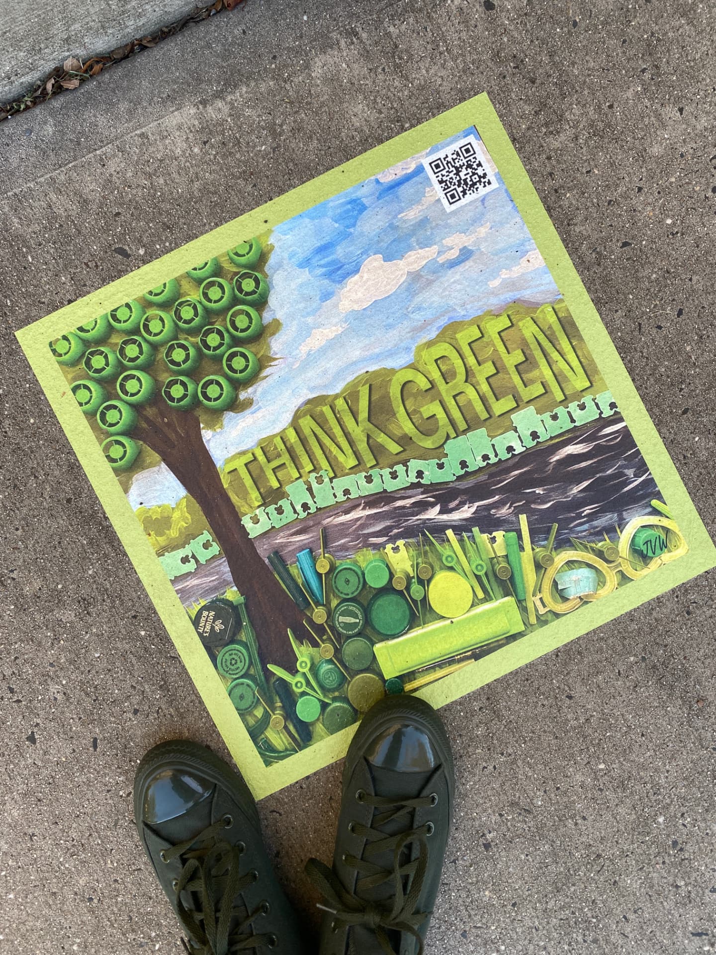 Think Green mixed-media artwork photographed on pavement, showing a bottle-cap tree, painted sky and river, green lettering, and a QR code sticker