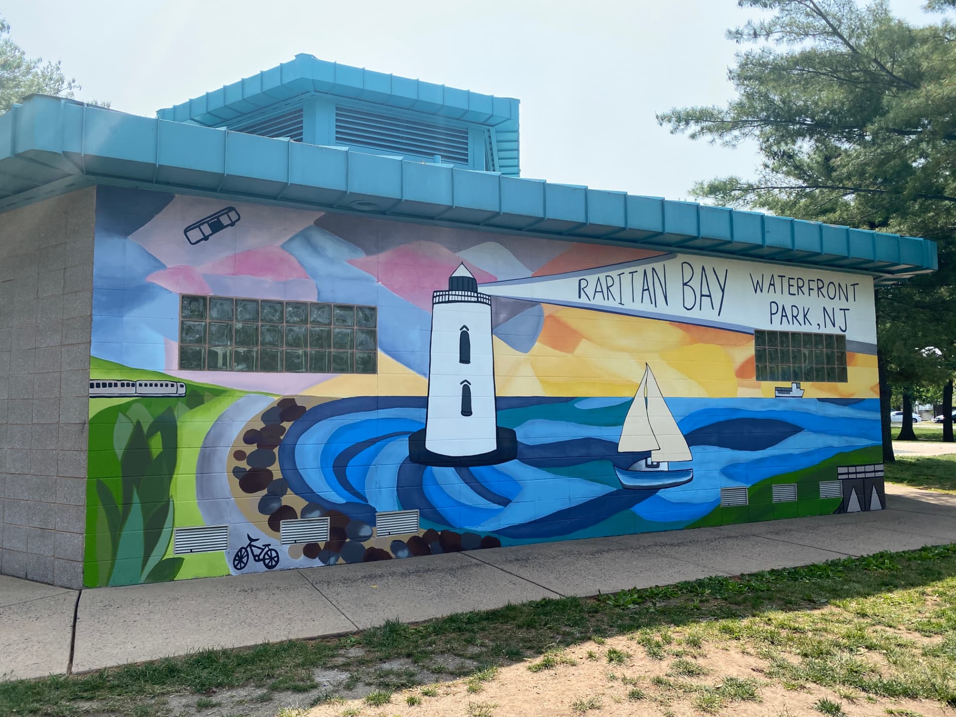 Painted mural on a park building showing a lighthouse, sailboat, waves and hand-lettered text reading Raritan Bay Waterfront Park NJ