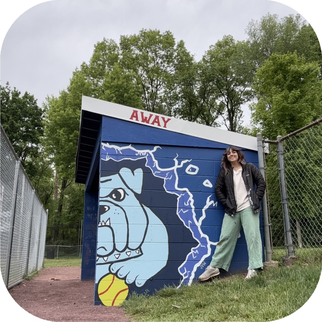 Julia standing beside a dugout she painted with a bulldog and lightning bolt mural